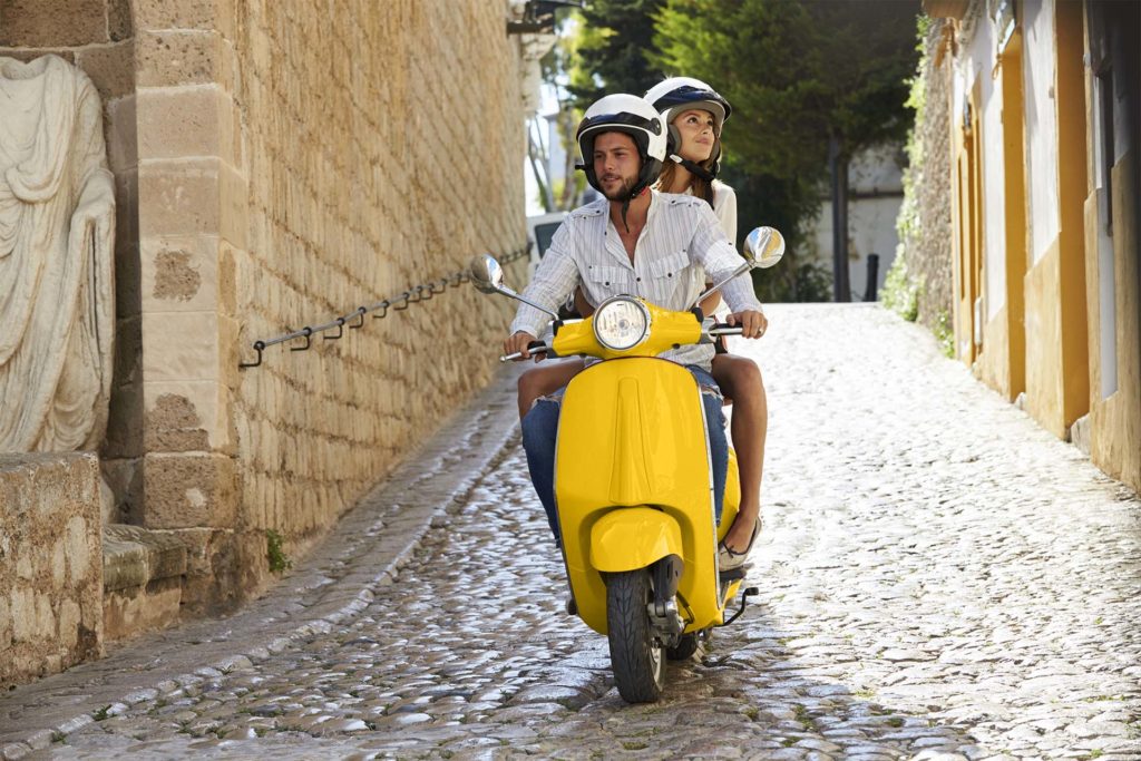 mann og dame på gul scooter i gate med brostein